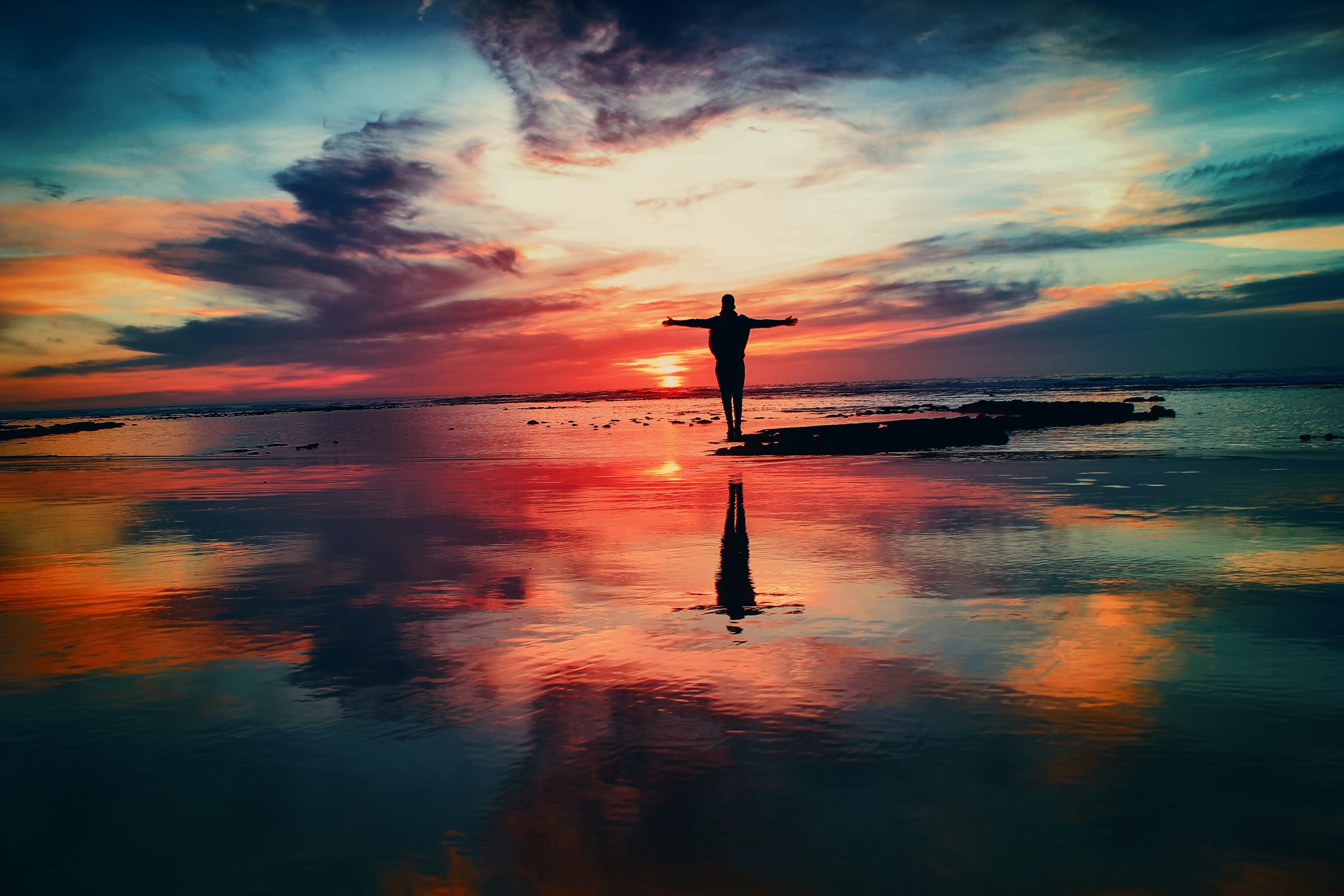 rainbow colored sunset reflecting in water with silhouette 